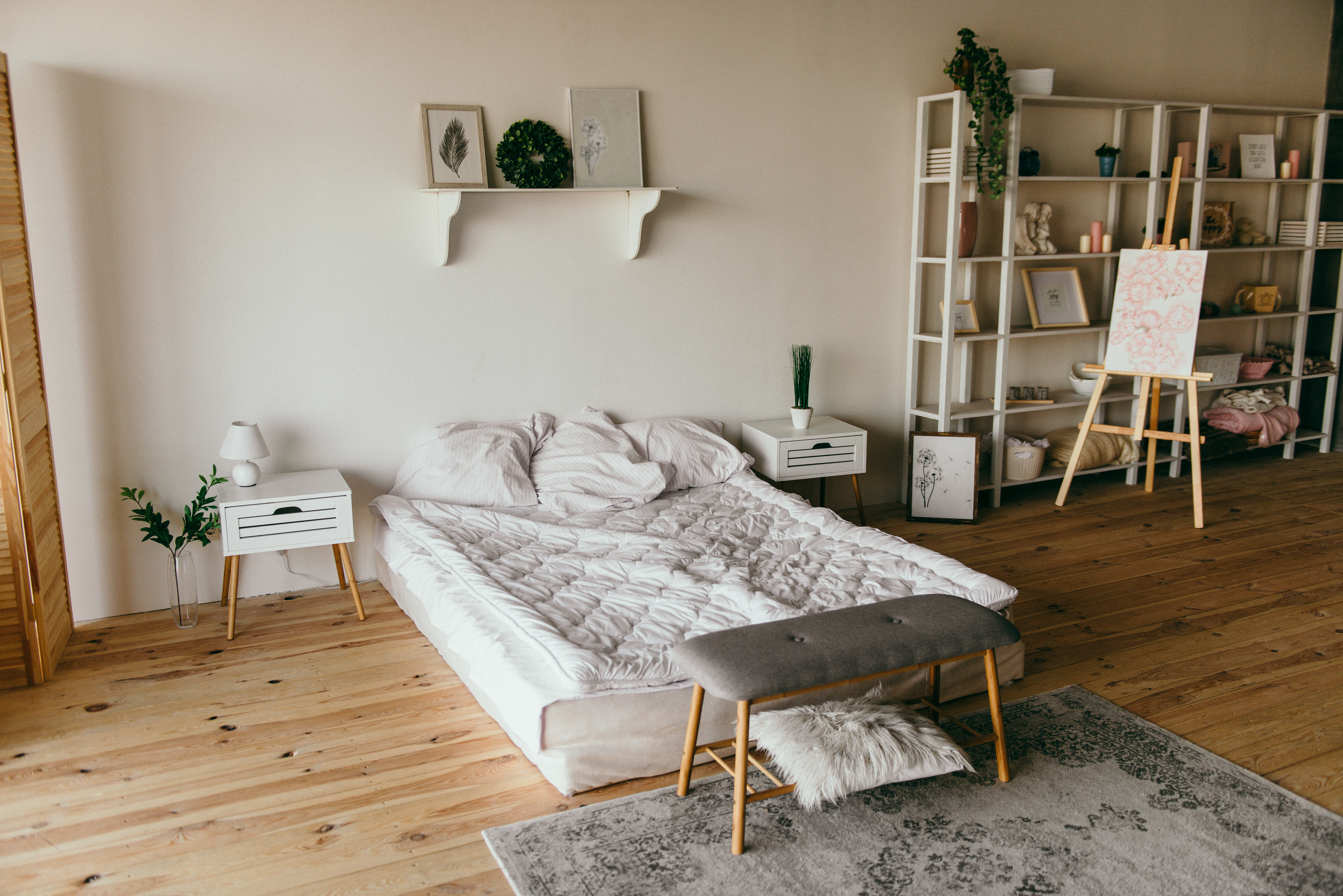 przestronna sypialnia z łóżkiem 200x220 w centrum pokoju. łóżko jest zaścielone prześcieradłem, leżą 3 poduszki, nad łóżkiem jest półka z książkami